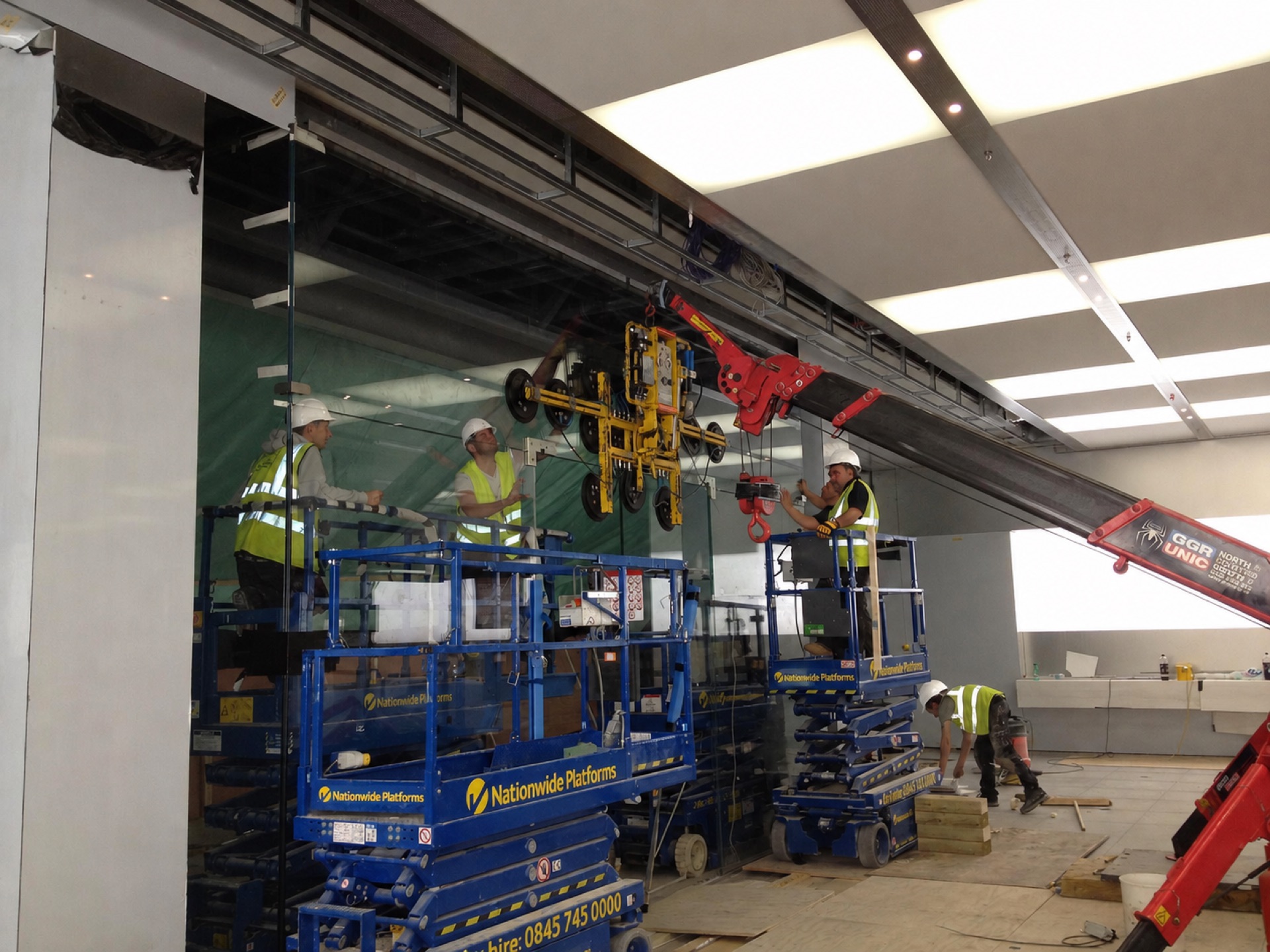 Mini-crane and vacuum lifter lifting a large glass panel into an Apple storefront during installation