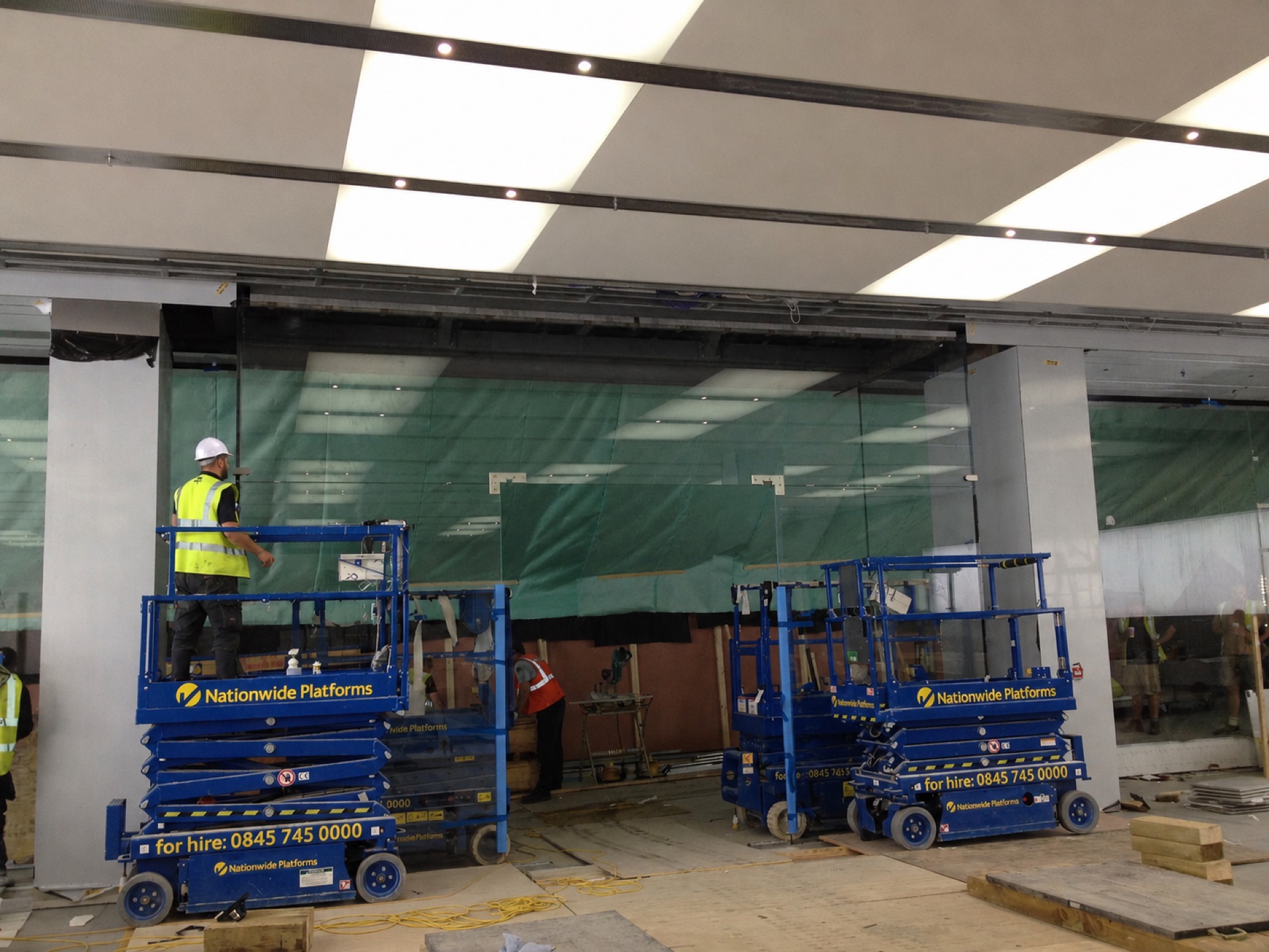 Installers on scissor lifts setting full-height glass panels in a shopping centre storefront