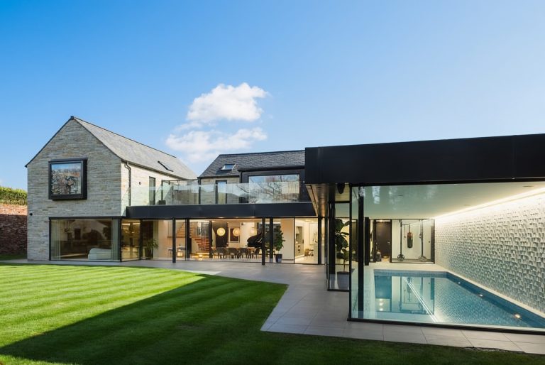 Rear elevation of a Rothwell home with full-height structural glazing and a glazed pool pavilion overlooking the lawn