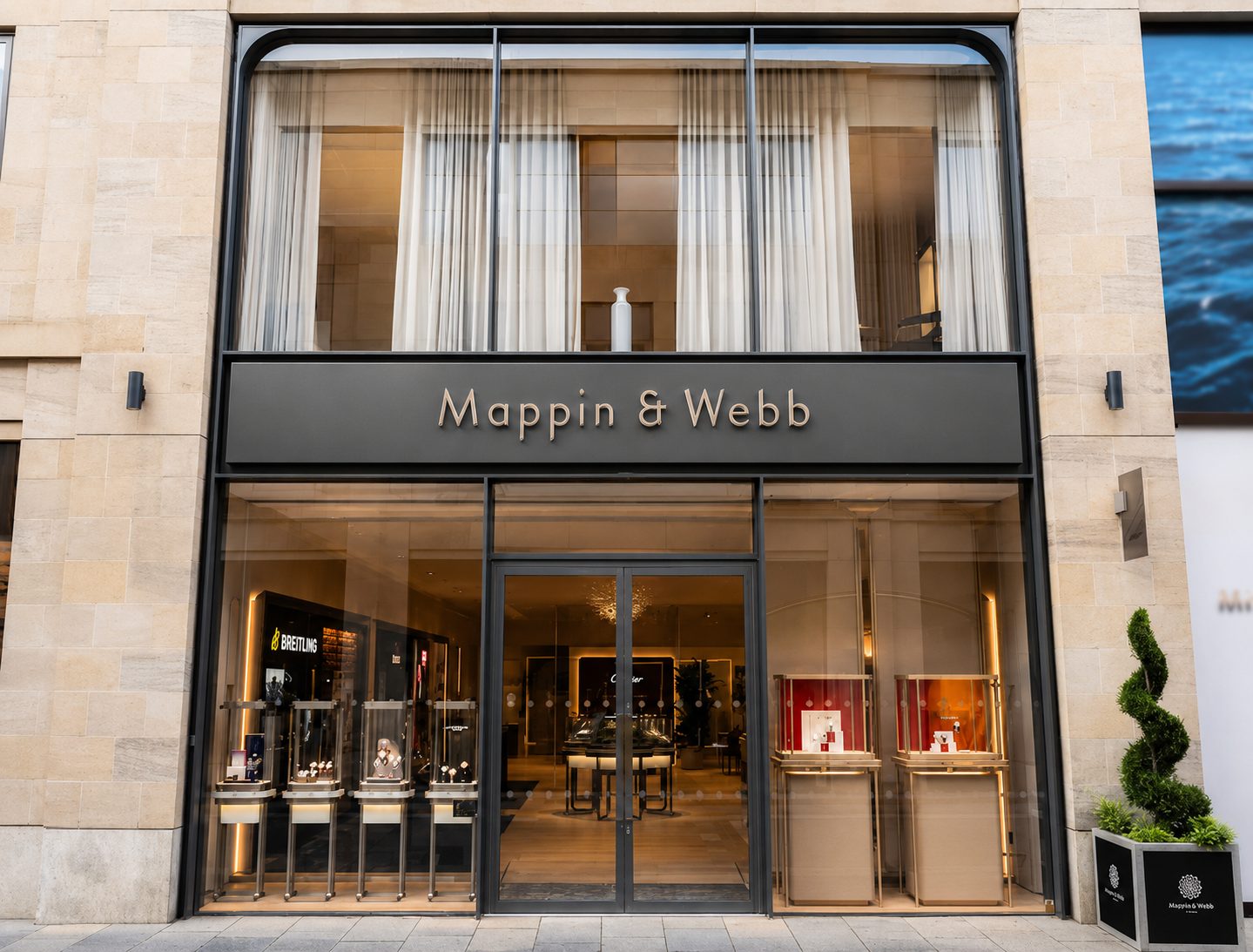 Bronze-framed jewellers shopfront with full-height glazing on a stone facade