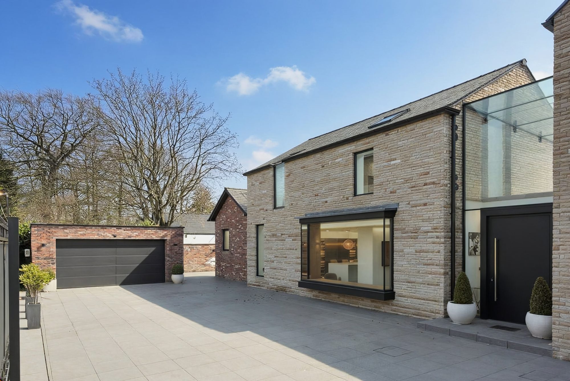 Stone house with slim aluminium windows and a glazed stairwell seen from the driveway