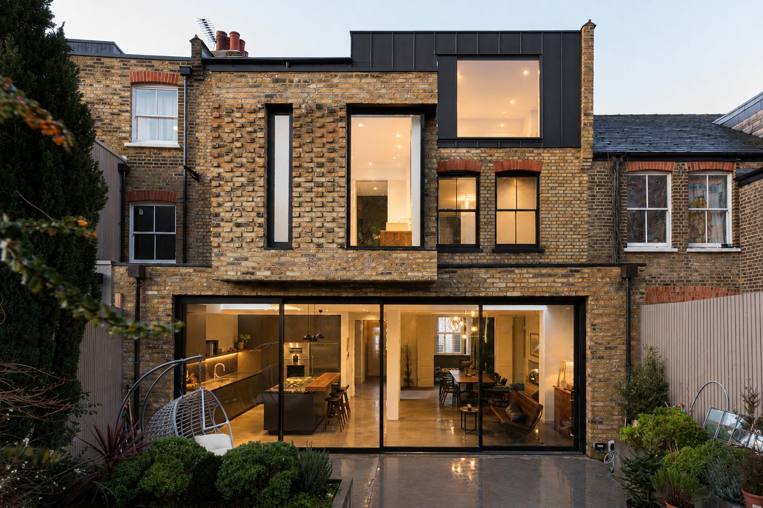 Rear elevation of a brick terraced house with aluminium sliding doors and rooflights at dusk